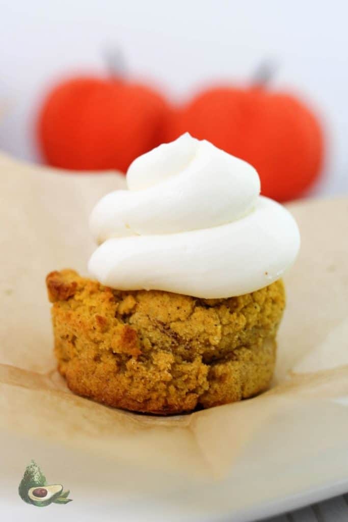 close up of keto pumpkin muffin with two pumpkins in the background