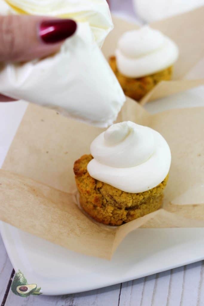 womans hand piping frosting on a low carb pumpkin muffin